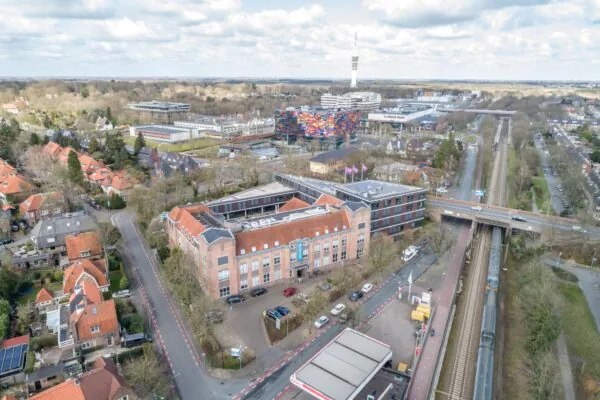 Luchtfoto van de Lage Naarderweg in Hilversum met uitzicht op het Media Park, het kleurrijke Instituut voor Beeld en Geluid en een passerende trein.